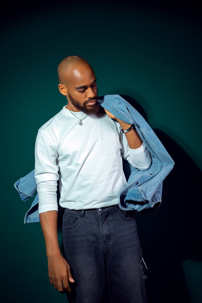 Moceol with a denim jacket draped over one shoulder, moody teal backdrop